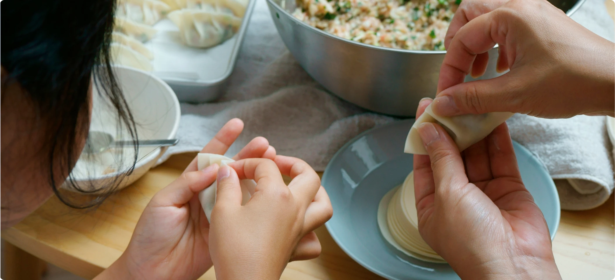 Adults and children folding dumplings together at a kitchen table.