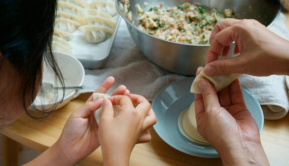 Adults and children folding dumplings together at a kitchen table.